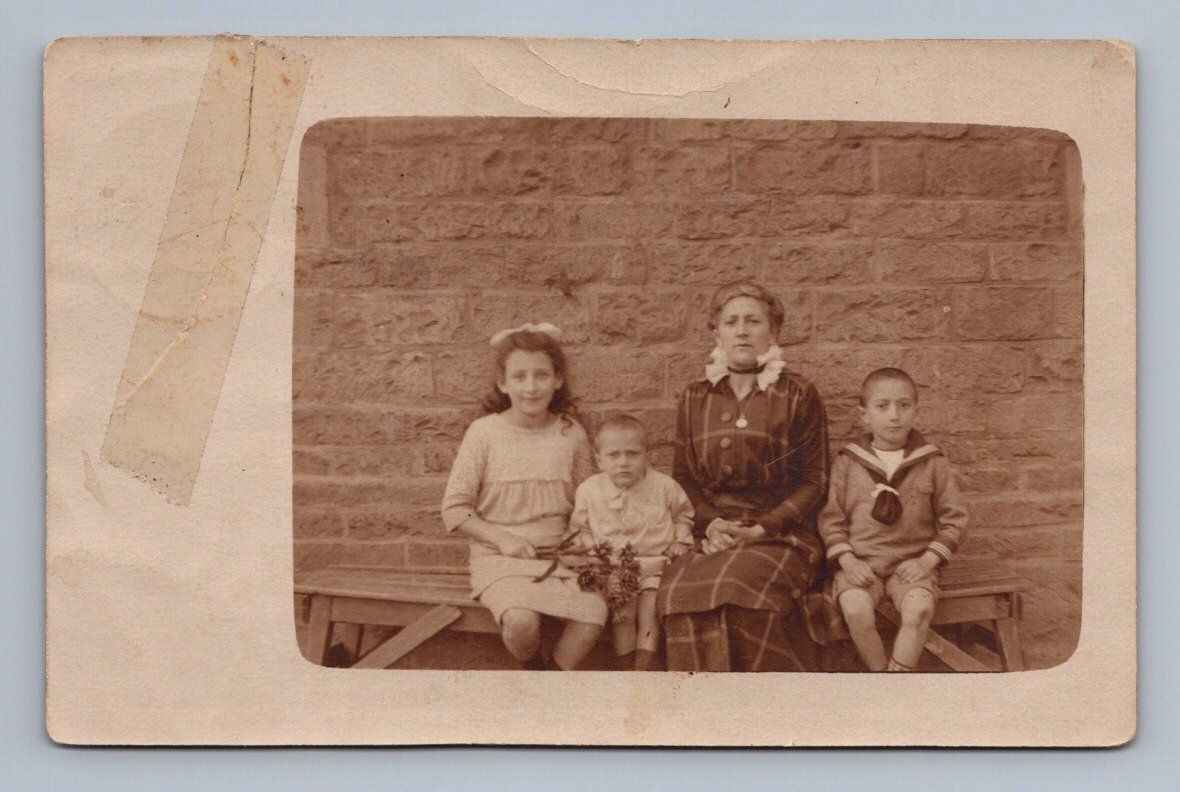 Family portrait three children mother seated in front of brick wall Rppc 1915
