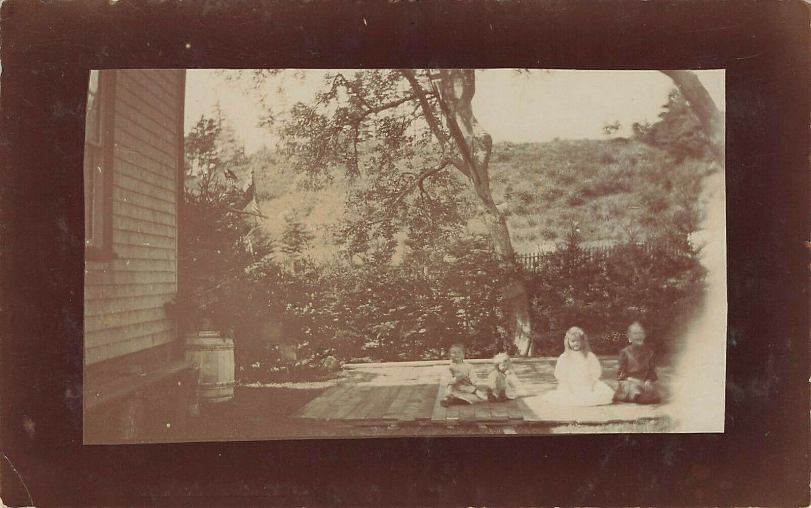 CHILDREN ON WOOD DECK WITH US FLAG IN BACKGROUND REAL PHOTO POSTCARD 1910s RPPC