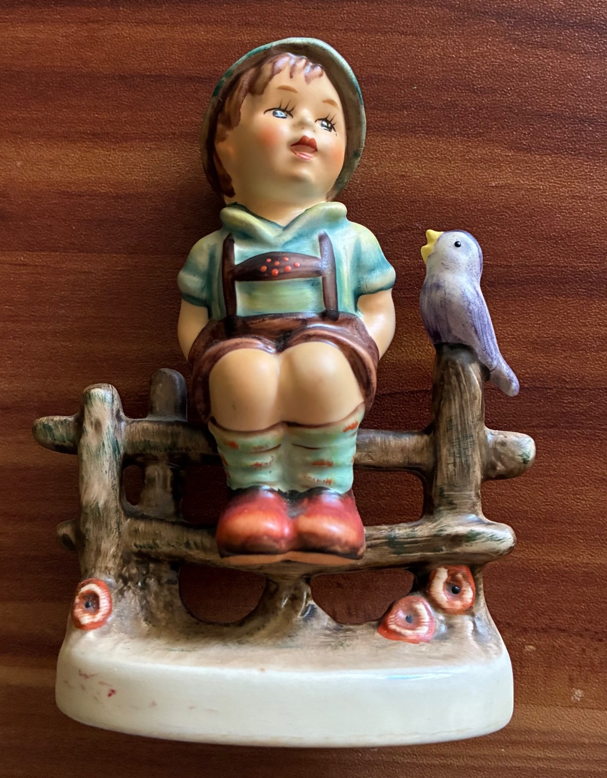 Bavarian boy sitting on a rustic fence next to a bird figurine \