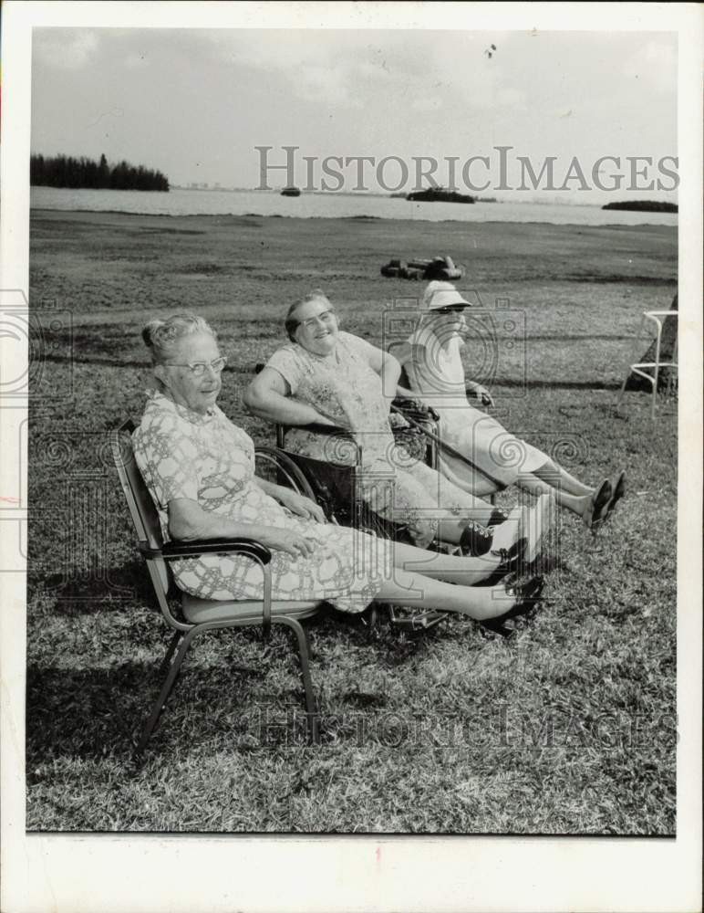 1975 Press Photo Three elderly ladies relaxing in field near the water