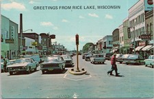Greetings Rice Lake Wisconsin Downtown Street Scene Postcard 1960s Cars picture